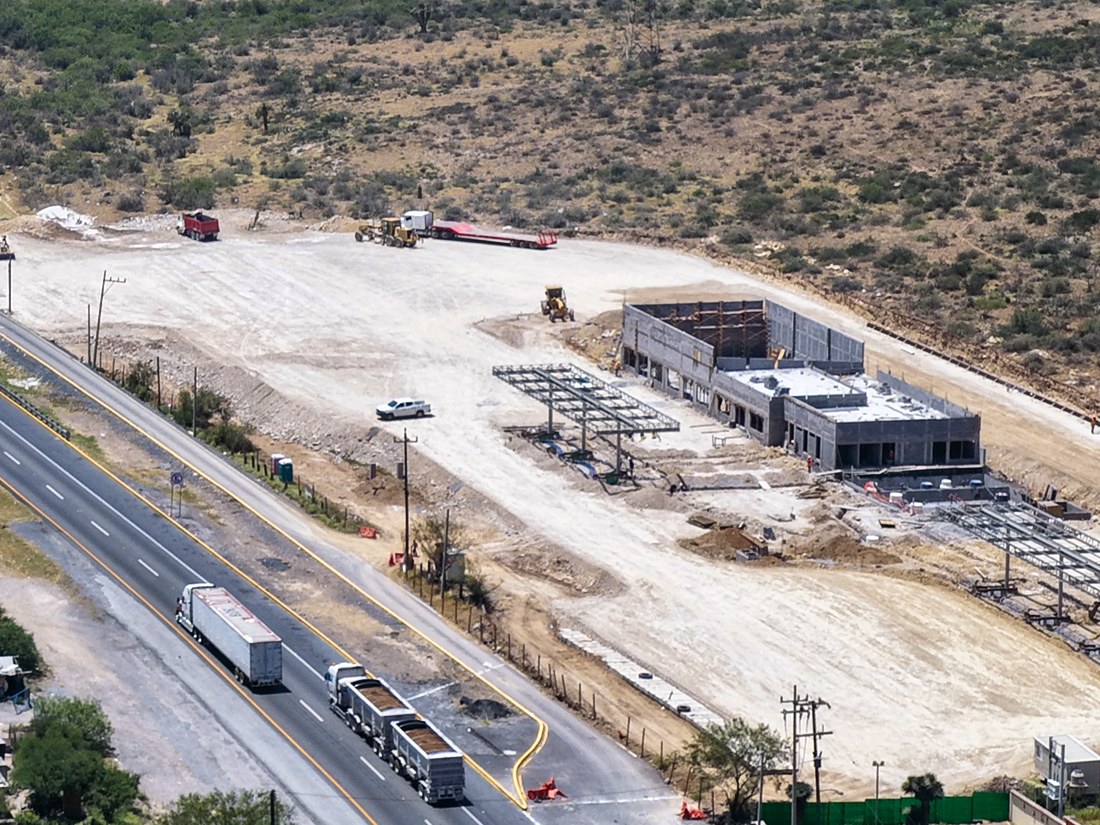 Plataforma de terracería y edificio en obra junto a una carretera, vistos desde el aire